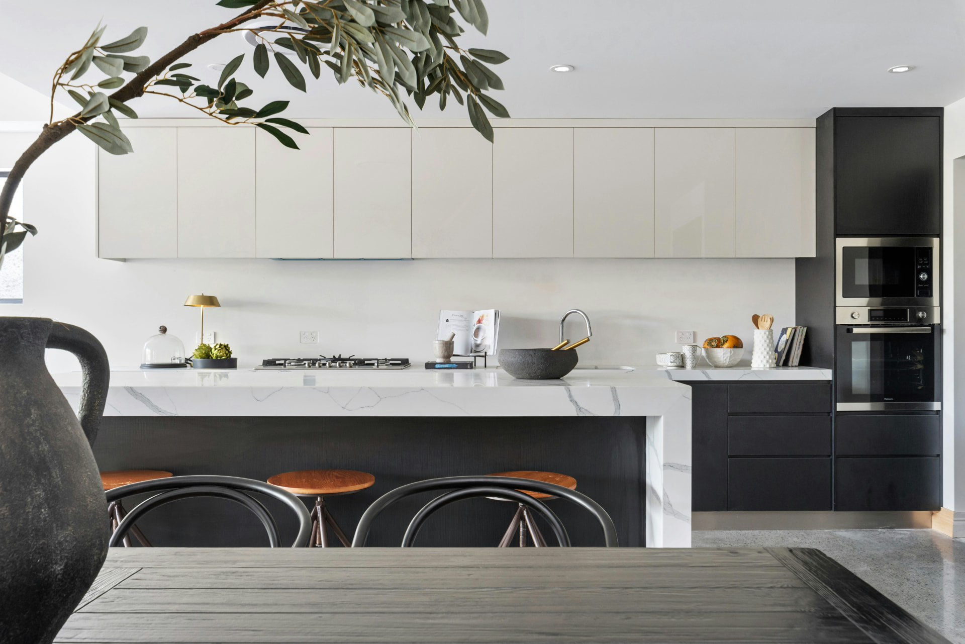 Modern kitchen with white flat-panel uppers, dark base cabinetry, and a marble waterfall island